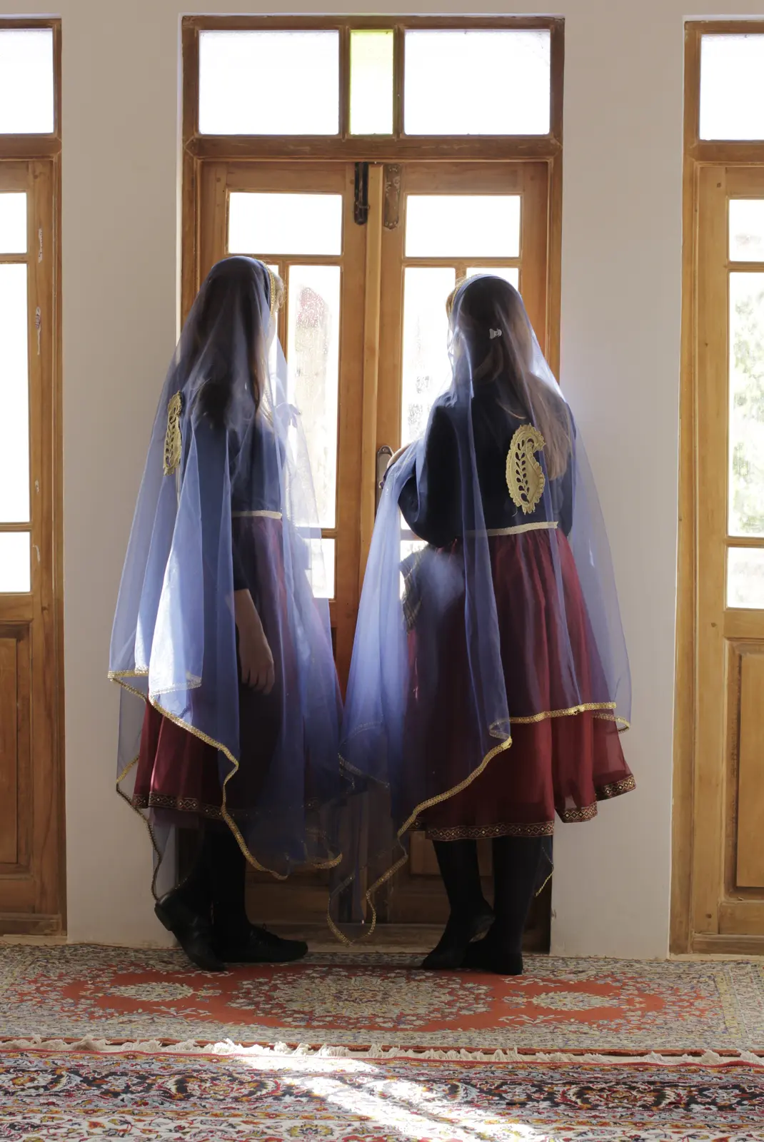 Two Miniature dancers in layered blue and burgundy costumes by tall windows